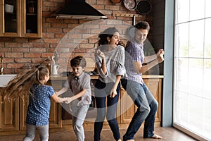 Overjoyed young family with kids dance in kitchen