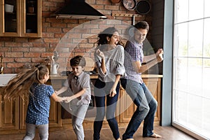 Overjoyed young family with kids dance in kitchen photo