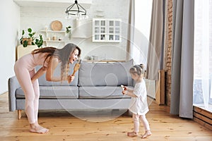 Overjoyed young mom or nanny have fun playing with cute little girl child, excited mother dancing