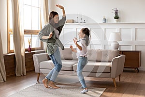 Overjoyed young mommy babysitter dancing to music with girl.