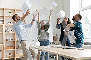 Overjoyed young multiracial business team throwing paper documents in air.
