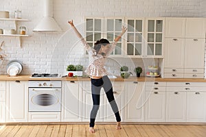 Overjoyed young woman dancing, jumping in modern kitchen at home