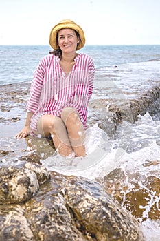 Overjoyed young woman laughing sitting on stone beach surrounded by water splashes foamy waves