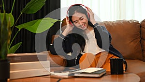 Overjoyed young woman listening to music on headphone while relaxing on couch at home