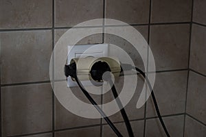 Overloaded outlet with an extension and many sockets plugged in, risk of fire and short circuit on a wall with tiles