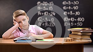 Overloaded schoolboy sitting at desk and failing to solve difficult equation