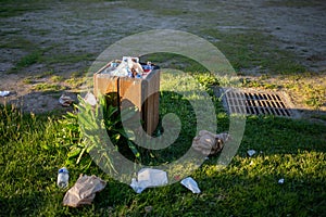 Overloaded trash container with plastic on grass, garbage dump in public zone, environmental problem