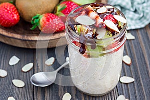 Overnight oatmeal with fresh strawberry and kiwi, garnished with chocolate sauce and sliced almond in glass jar