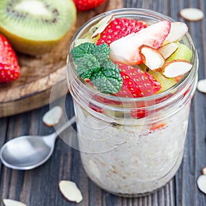 Overnight oatmeal with fresh strawberry and kiwi, garnished with sliced almond in glass jar, square