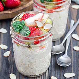 Overnight oatmeal with fresh strawberry and kiwi, garnished with sliced almond in glass jar, square format