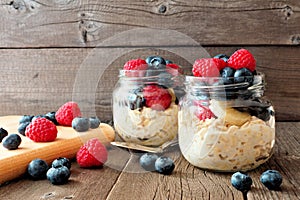 Overnight oats with blueberries and raspberries in jars on rustic wood