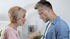 Overprotective mother feeding her adult son with spoon, relations in family