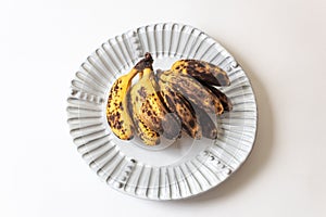 Overripe baby bananas on a fluted white plate, isolated on white