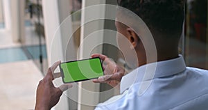 Overshoulder view of afro american guy holding phone in horizontal landscape mode. Guy looking and touching green