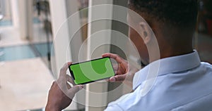 Overshoulder view of afro american man holding smartphone in horizontal landscape mode. Guy looking at mock up phone
