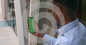 Overshoulder view of afro american man holding smartphone and touching green screen while making yes gesture. Chroma key