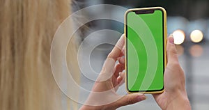 Overshoulder view of unknown woman holding smartphone green screen with both hands. Close up view of female person using