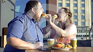 Oversize couple sharing burgers during romantic date outdoors, calories and diet