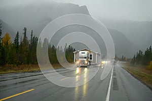 An oversize load truck carrying a prefabricated mobile home in extremely bad weather on a rainy day on a Canadian highway