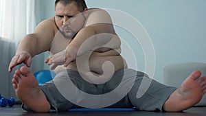 Oversize man stretching on mat trying to reach toes, improving muscle elasticity