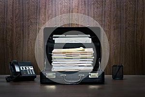 Overtime! Tall stack of files and folders in black leather briefcase on desk with phone