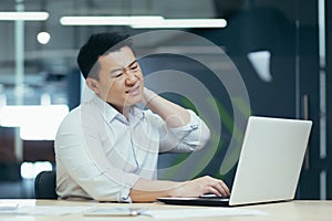 Overtired asian worker in office, having severe neck pain photo