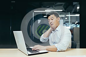 Overtired asian worker in office, having severe neck pain photo