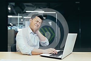 Overtired asian worker in office, having severe neck pain photo