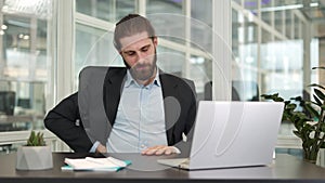 Overtired businessman feeling back pain while working with laptop in own cabinet