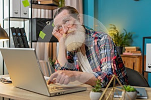 Overtired sleepy lazy senior man grandfather bored working on laptop while sitting in home office photo