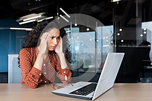 Overtired hispanic business woman working inside modern office, office worker with laptop having severe headache photo