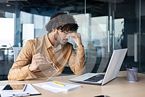 Overtired office worker in glasses working inside office with laptop, businessman manager working late. photo