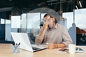 Overtired office worker in glasses working inside office with laptop, businessman manager working late photo