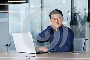 Overtired office worker at work with laptop inside office, man has severe neck pain, Asian man works long time sitting. photo