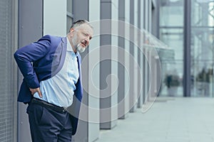 Overtired senior gray-haired man outside office building, businessman in business suit photo