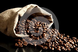 Overturned bag full of coffee beans on black