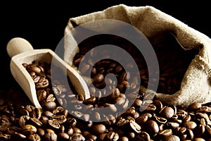 Overturned bag full of coffee beans on black with spatula