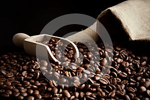 Overturned bag full of coffee beans on black with spatula