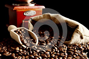 Overturned bag full of coffee beans on black with spatula and mill photo