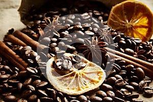 Overturned bag full of coffee beans,dried oranges on black