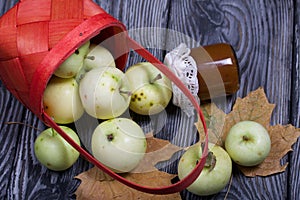 An overturned basket of apples. Nearby are jam, apples and dried maple leaves. Fruit harvest