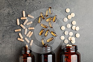 Overturned bottles with different dietary supplements on grey table, flat lay