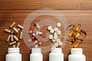 Overturned bottles with different dietary supplements on wooden table, flat lay. Space for text