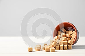 Overturned bowl with brown sugar cubes on white wooden table, space for text