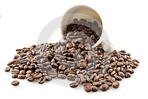 Overturned cup full of coffee beans on white