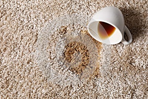 Overturned cup and spilled coffee on beige carpet, above view. Space for text