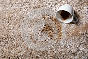 Overturned cup and spilled coffee on beige carpet, above view. Space for text