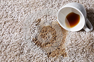 Overturned cup and spilled coffee on beige carpet, closeup