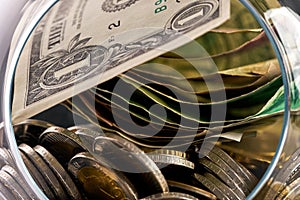 Overturned glass piggy box full of shined Golden coins and different paper currency banknotes