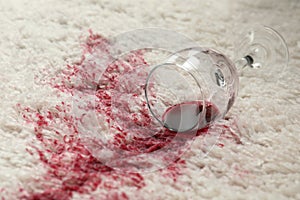 Overturned glass and spilled red wine on white carpet